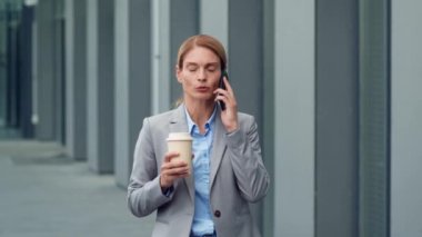 Busy business lady talking with partners on phone, spending her coffee break outdoors near office building, discussing project details, slow motion, free space