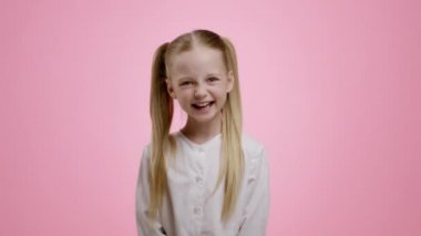 Sincere kid happiness. Adorable little girl with two ponytails laughing loud, pink studio background, slow motion