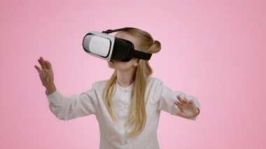 Children and modern technologies. Adorable little girl wearing VR headset enjoying virtual reality game, pushing and punching invisible objects, pink studio background