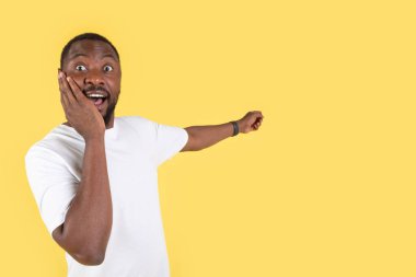 Wow Offer. Emotional African American Millennial Man Pointing Finger Aside At Empty Space For Text Posing Over Yellow Studio Background. Omg, Look There Concept