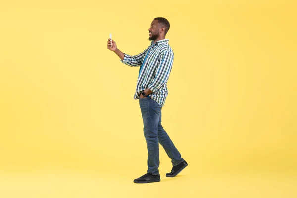 African American Male Using Phone Posing Walking Yellow Background Studio — Stockfoto