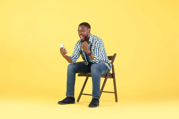 African American Guy Using Phone Shaking Fists Joy Sitting Chair — Fotografia de Stock