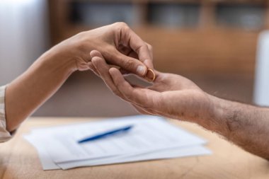 Hand of adult caucasian female gives ring to her ex husband at table with divorce papers, close up, cropped, free space. Relationship problems, disagreement, quarrel and break up, end of marriage