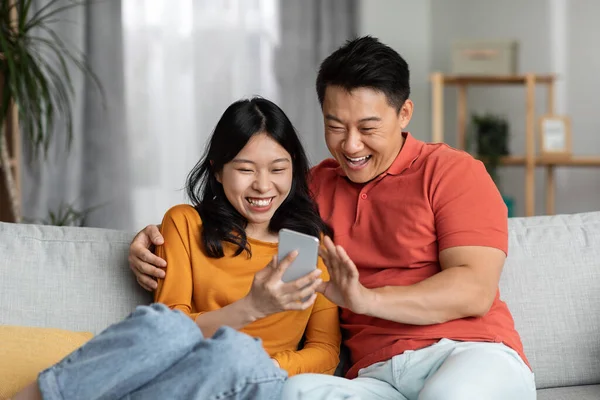Cheerful Chinese Spouses Man Woman Homewear Sitting Couch Using Cell — Fotografia de Stock