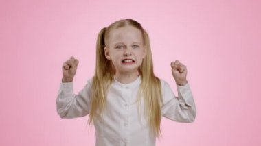 Kid emotional outburst. Angry little girl screaming loud and gesturing with fists, expressing her negative emotions, pink studio background, slow motion