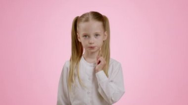 Kids and privacy. Studio portrait of mysterious little girl with ponytails zipping her lips and showing hush gesture, pink background, slow motion