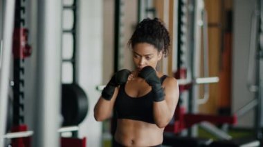 Female self defence. Young sporty african american woman practicing punches, training at gym interior, slow motion, free space