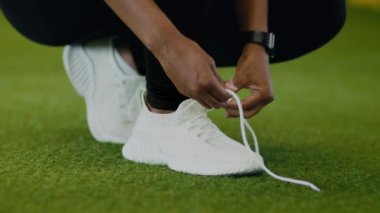 Preparing for sport workout. Close up shot of unrecognizable black lady tying up laces on her sneakers, fixing shoes at gym, slow motion
