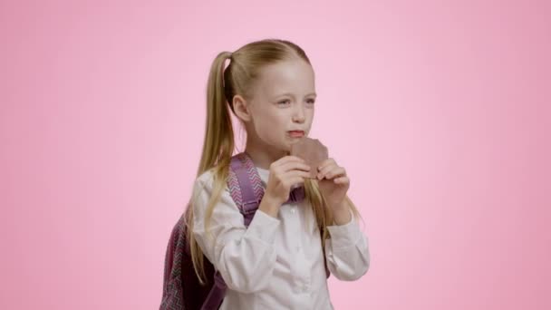 Солодкий Перекус Емоційна Маленька Школярка Рюкзаком Кусає Шоколадний Батончик Насолоджуючись — стокове відео