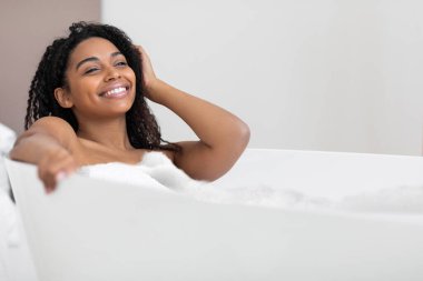 Pamper Time. Happy Black Female Relaxing In Bathtub With Foam At Home, Smiling Young African American Woman Taking Hot Bath With Soap Bubbles, Enjoying Domestic Spa, Closeup Shot With Copy Space