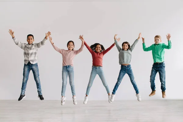 Group Joyful Diverse Kids Jumping Raising Arms Smiling Camera Celebrating — Fotografia de Stock