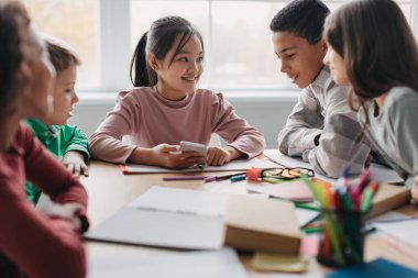 Happy Multicultural School Children Using Phone Together Having Fun During Break In Classroom. Educational Application For Cellphone, Kids And Gadgets Concept. Selective Focus