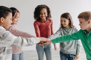 Kids Teamwork And Unity. Happy Preteen Children Stacking Hands Together Standing In Circle Indoors. Teambuilding And Friendship Concept. Selective Focus