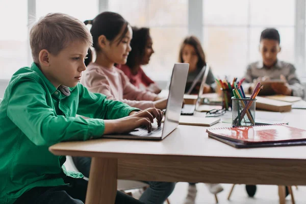 Learning Blonde Boy Using Laptop Sitting Multiethnic Classmates Modern Classroom —  Fotos de Stock