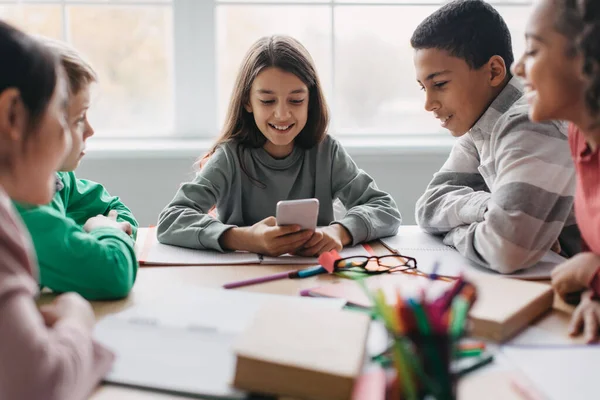 Cheerful Diverse School Children Using Cellphone Sitting Desk Modern Classroom —  Fotos de Stock
