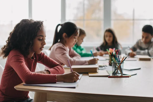 African American Schoolgirl Taking Notes Writing Essay Learning Sitting Diverse —  Fotos de Stock