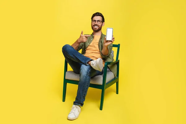 Happy Man Casual Wear Pointing Cellphone Empty Screen Sitting Armchair — Stockfoto