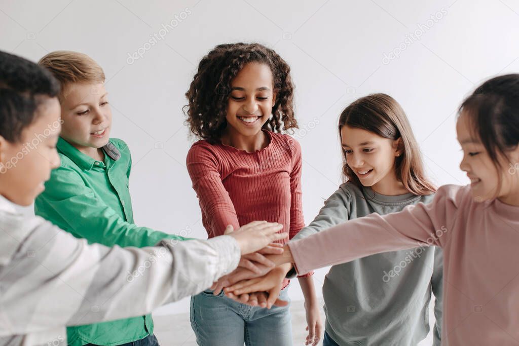 Teambuilding. Cheerful Multiracial Kids Putting Hands Together Standing In Circle Symbolizing Unity And Friendship Posing Indoors. Preteen Boys And Girls Stacking Arms. Selective Focus