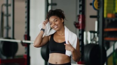 Effective training. Close up portrait of happy tired african american lady athlete wiping her sweating forehead with towel, feeling satisfied of intensive workout at gym, slow motion