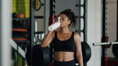 Sports and water balance. Young pretty african american woman athlete drinking water, hydrating body during workout at gym, slow motion, free space
