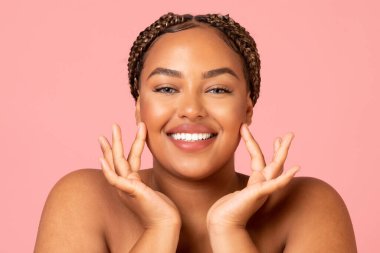 Facial Skincare. Attractive Black Woman Touching Face Moisturizing Smooth Skin Posing Smiling To Camera Over Pink Background In Studio. Beauty Routine And Pampering Concept
