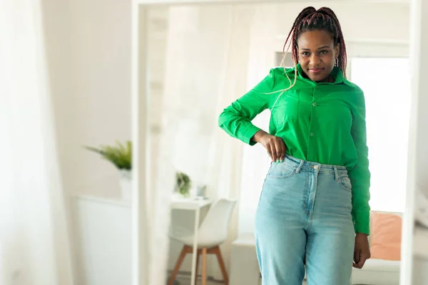 Excited fit african american woman after great weight loss, wearing jeans, looking at her reflection in mirror and smiling, copy space. Healthcare and beauty care