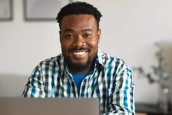 Freelance. Cheerful African American Male Using Laptop Computer Smiling To Camera Working Online Sitting At Desk Indoor. Distance Job And IT Career Concept. Selective Focus