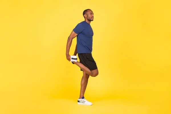 Sporty African American Male Exercising Stretching Leg Standing Yellow Studio — Stockfoto