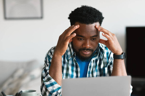 Thoughtful African American Man Using Laptop Computer Working Online And Thinking About Business Problems Touching Head Sitting Indoors. Entrepreneurship Issues Concept. Selective Focus