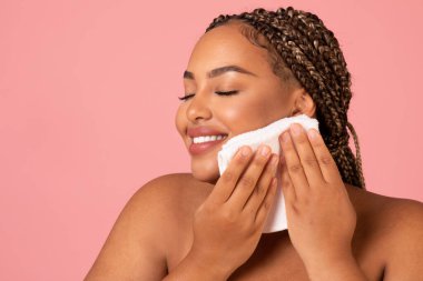 Portrait Of Happy African American Lady Drying Face With Soft Towel Caring For Skin Posing Over Pink Studio Background. Facial Skincare And Pampering Concept