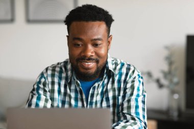 Happy Black Male Freelancer Using Laptop Working Remotely And Browsing Internet Sitting At Desk At Home. Freelance And Internet Entrepreneurship Concept. Front View