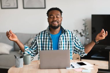 Relaxed African American Man Meditating At Laptop Calming Down Relaxing With Eyes Closed At Workplace Sitting At Desk Indoor. Online Yoga, Relaxation And Mindfulness