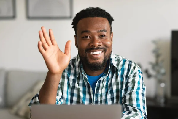 Hello. Happy Black Freelancer Guy Waving Hand To Camera Sitting At Laptop Computer Video Calling Communicating Online At Home. Remote Job And Communication Concept