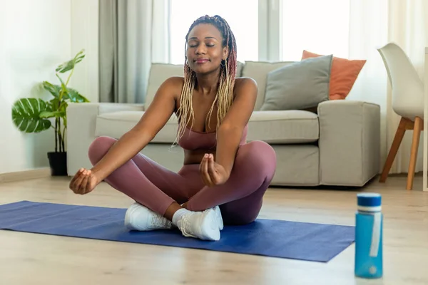 Mental health. Black lady with closed eyes meditating at home, sitting on floor fitness mat in living room, copy space. Calm woman practicing yoga, leading healthy lifestyle