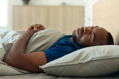 Peaceful African American Man Enjoying Healthy Sleep Resting In Cozy Bed Lying In Bedroom. Guy Napping At Home At Daytime. Recreation And Sleeping Routine Concept. Selective Focus