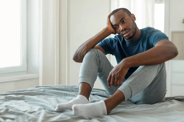 Male Depression Problem. Unhappy Black Male Thinking About Loneliness Sitting On Bed In Modern Bedroom Indoors. Negative Thoughts And Mental Health Issues Concept