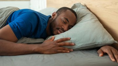 African American Guy Sleeping Peacefully Embracing Pillow Lying In Modern Bedroom Indoors. Man Enjoying Daytime Sleep Napping In Bed Indoors. Recreation Concept. Panorama