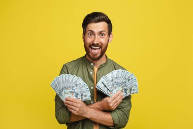 Big luck and win concept. Portrait of happy man holding a lot of dollar cash, celebrating success and posing with money over yellow studio background