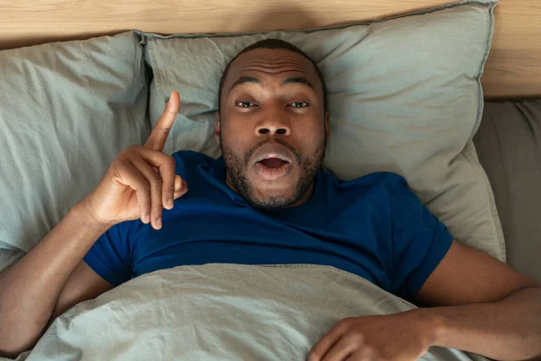 I Have Idea. Sleepy Black Guy Pointing Finger Up Looking At Camera, Having Inspiration Lying In Bed In Modern Bedroom At Night. Eureka Moment Concept. High Angle View