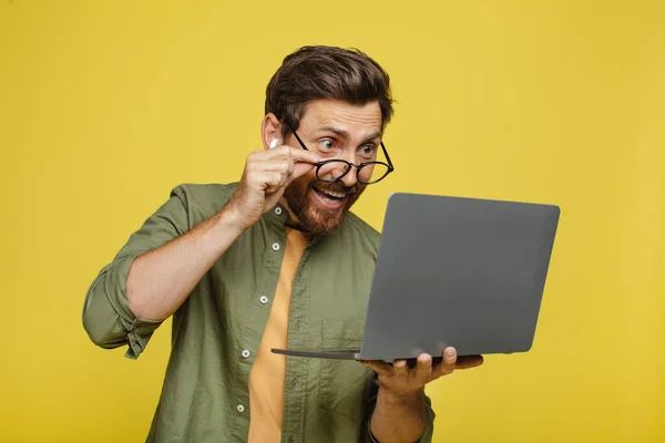 Overjoyed middle aged man looking at laptop screen, opening mouth in shock, excited about win or success on yellow background. Male with portable pc cannot believe huge online sale