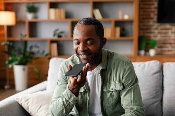 Cheerful middle aged african american male calling by smartphone with blank screen in living room interior. Communication remotely, new normal with technology, app for talking with client at home
