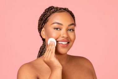 Facial Skincare. Smiling Black Woman Using Cotton Pad Caring For Smooth Skin Looking At Camera Posing Over Pink Background In Studio. Beauty And Cosmetics Concept