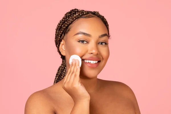 Facial Skincare. Smiling Black Woman Using Cotton Pad Caring For Smooth Skin Looking At Camera Posing Over Pink Background In Studio. Beauty And Cosmetics Concept