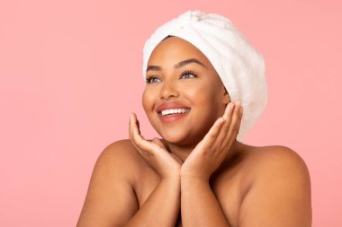 Facial Skincare. Portrait Of Overweight Black Woman Posing Holding Hands Near Face Looking Aside Caring For Skin Standing Wrapped In Towel In Studio On Pink Background. Beauty And Pampering