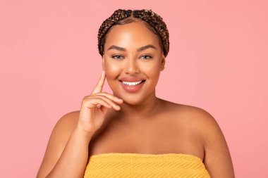 Portrait Of Attractive Obese Black Woman Touching Face Posing Smiling To Camera Over Pink Studio Background, Standing Wrapped In Towel. Beauty, Wellness And Spa Concept