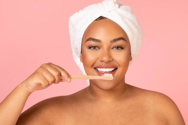Portrait Of African American Lady Brushing Teeth Posing With Toothbrush Smiling To Camera Standing Posing With Wrapped Towel On Head Over Pink Studio Background. Healthy Teeth And Oral Hygiene