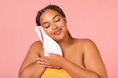 Pretty Overweight Black Lady Drying Face With Soft White Towel Enjoying Facial Skincare Routine Posing Standing Over Pink Background In Studio. Skin Care And Pampering Concept