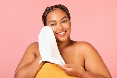 Facial Skincare. Plus Size Black Woman Drying Face With Soft Towel Smiling To Camera Posing Over Pink Background In Studio. Beauty Care Routine And Spa Concept