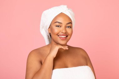 Cheerful Plump African American Lady Posing Smiling To Camera Touching Face Standing Wrapped In Towel Over Pink Background. Studio Shot Of Attractive Plus Size Female. Body Positive Concept