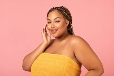 Female Beauty. Pretty Obese Black Lady Wrapped In Towel Posing Touching Face Smiling Looking At Camera Standing Over Pink Studio Background. Body Positive Concept